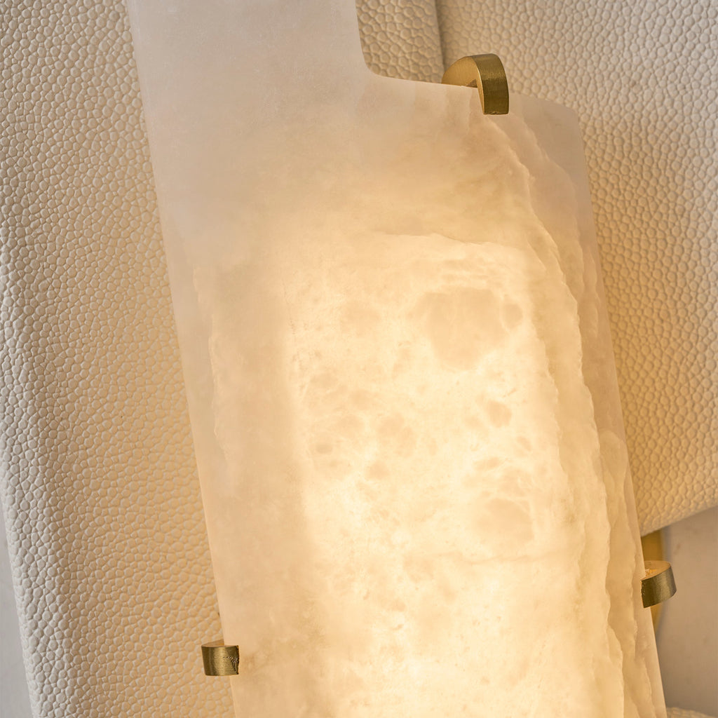 Close view of the lit alabaster slab on this Clérachic wall lamp, held in place by small brass clips on a pebbled panel.