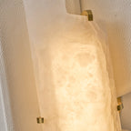 Close view of the lit alabaster slab on this Clérachic wall lamp, held in place by small brass clips on a pebbled panel.