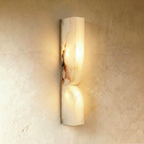 Clérachic taller double-curved alabaster wall light lit warm on a slim gold backplate, veining glowing on a plaster wall.