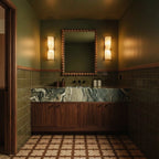 Pair of Clérachic alabaster wall lights flanking a beaded wooden mirror in a green tiled room with a marble counter.