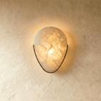 Clérachic alabaster wall sconce glowing warm on a limewashed wall, its veined stone held in a slim dark metal arc.