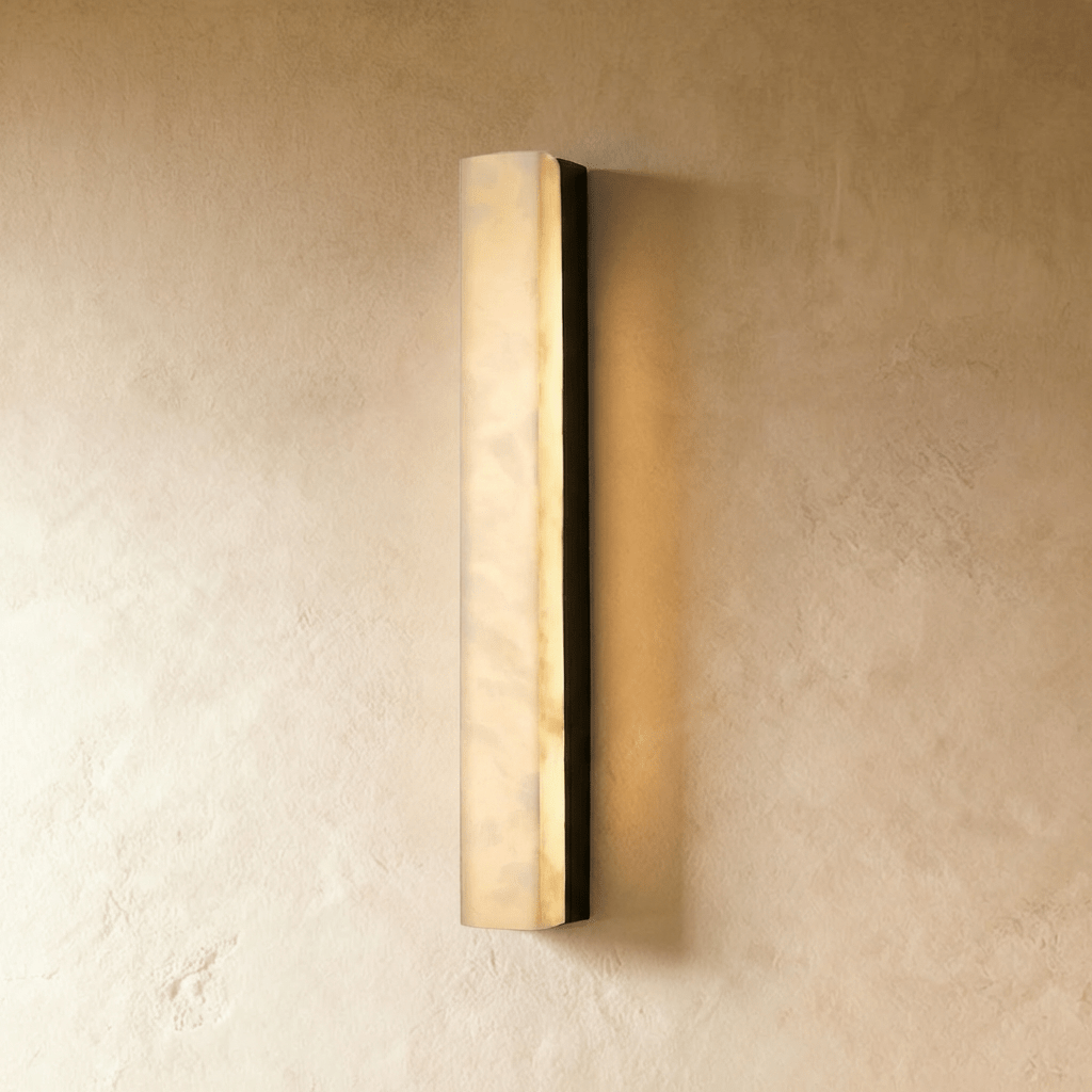 Clérachic slim rectangular alabaster wall light in a black metal frame, softly glowing on a warm limewash wall in the studio.