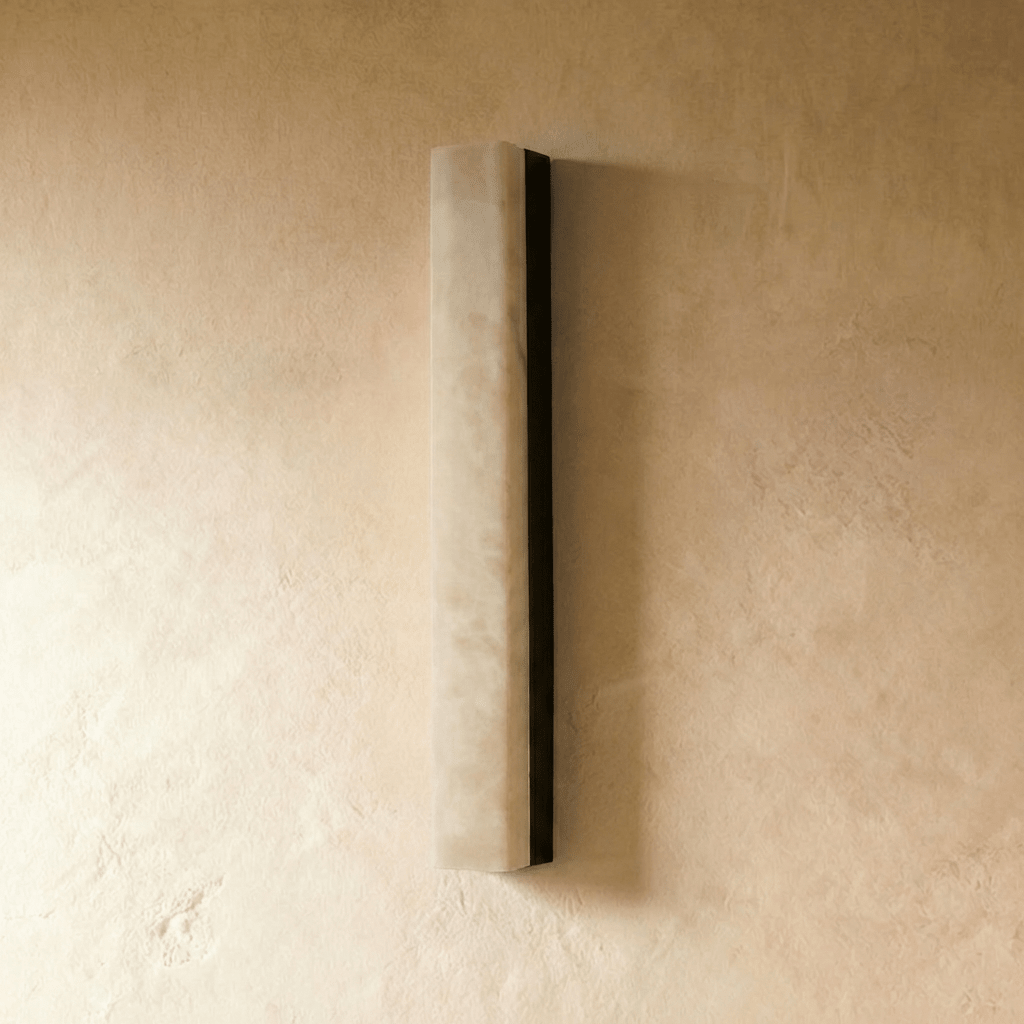 Clérachic tall alabaster bar wall light with a black metal backing, unlit, mounted on a pale limewash wall in a studio shot.