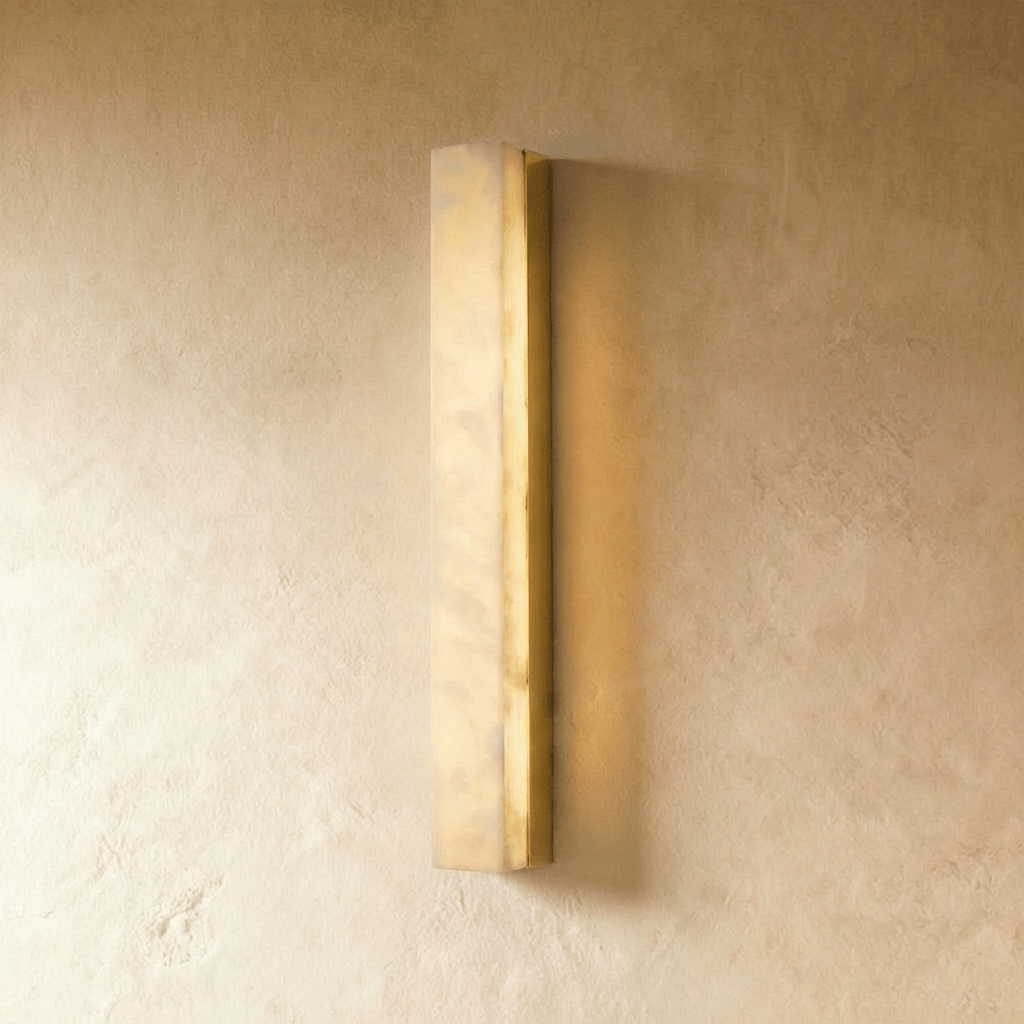 Clérachic slim alabaster bar wall light in a brushed gold frame, glowing gently against a warm limewash wall in the studio.