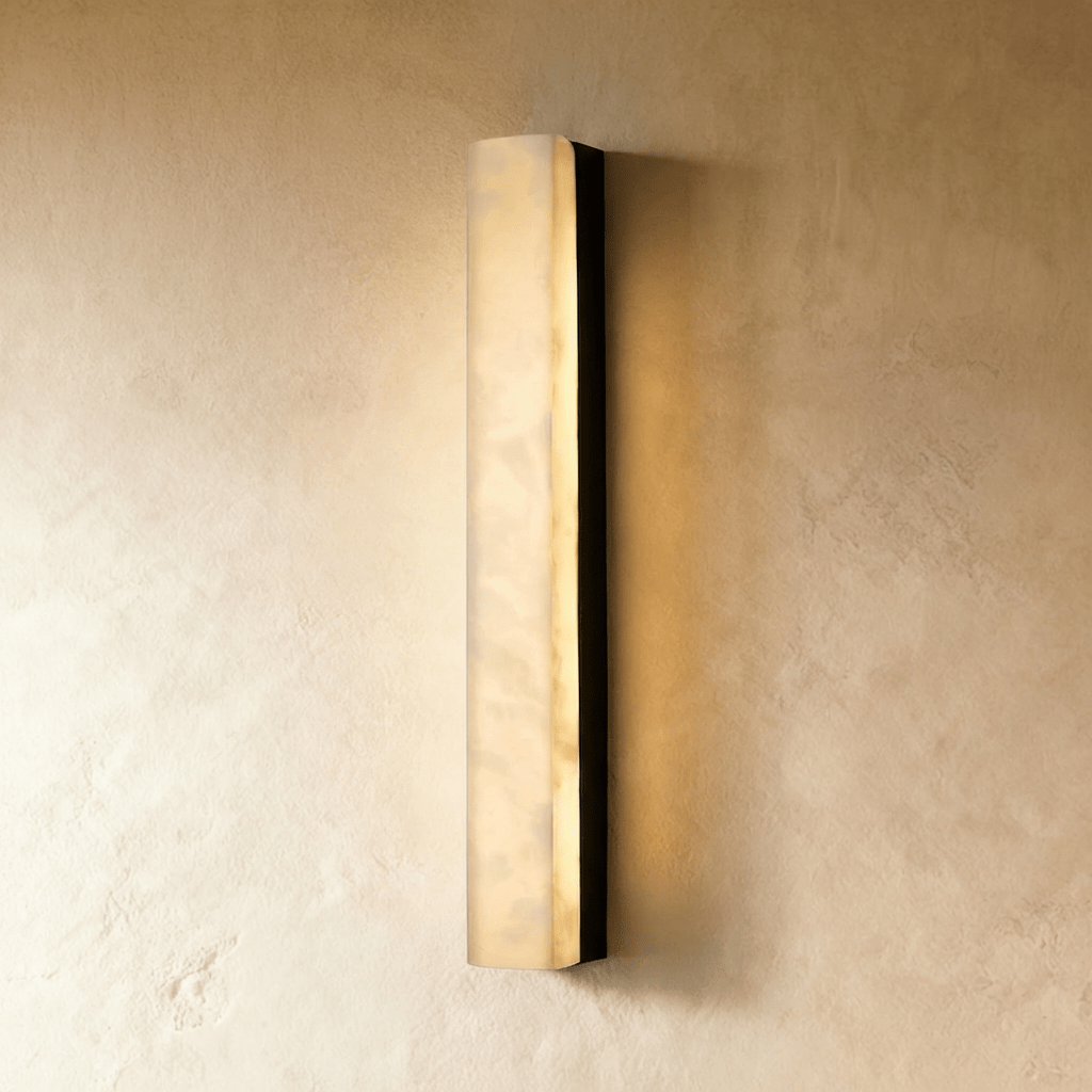 Clérachic medium-length alabaster wall light with a black metal frame, lit with a warm glow on a textured limewash wall.