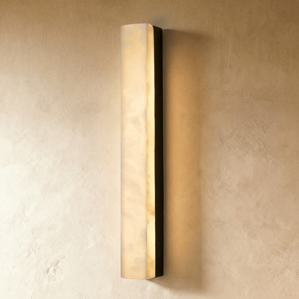 Clérachic long alabaster bar wall light with a black frame, lit from within and mounted on a limewash wall in the studio.