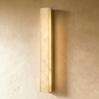 Clérachic long alabaster bar wall light in a gold frame, glowing warmly on a textured limewash wall in a studio shot.