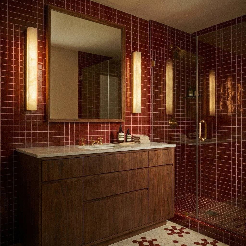 Clérachic alabaster bar wall lights beside a mirror on deep red tiles, with a timber cabinet and a glass shower in the room.