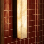 Close up of a Clérachic lit alabaster bar wall light with a black frame against glossy red tiles beside a timber mirror edge.