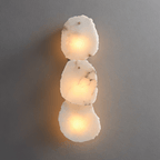 Clérachic three-light wall lamp, stacked rough-cut alabaster panels lit warm white on a plain grey wall.