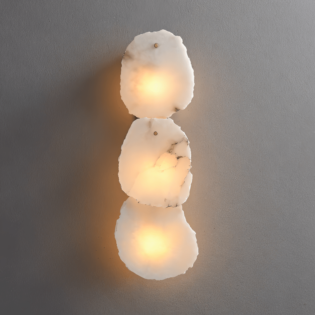 Clérachic three-light wall lamp, stacked rough-cut alabaster panels lit warm white on a plain grey wall.