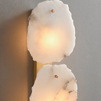 Close view of a Clérachic alabaster wall lamp, glowing marble panels with brass pins on a brass plate.