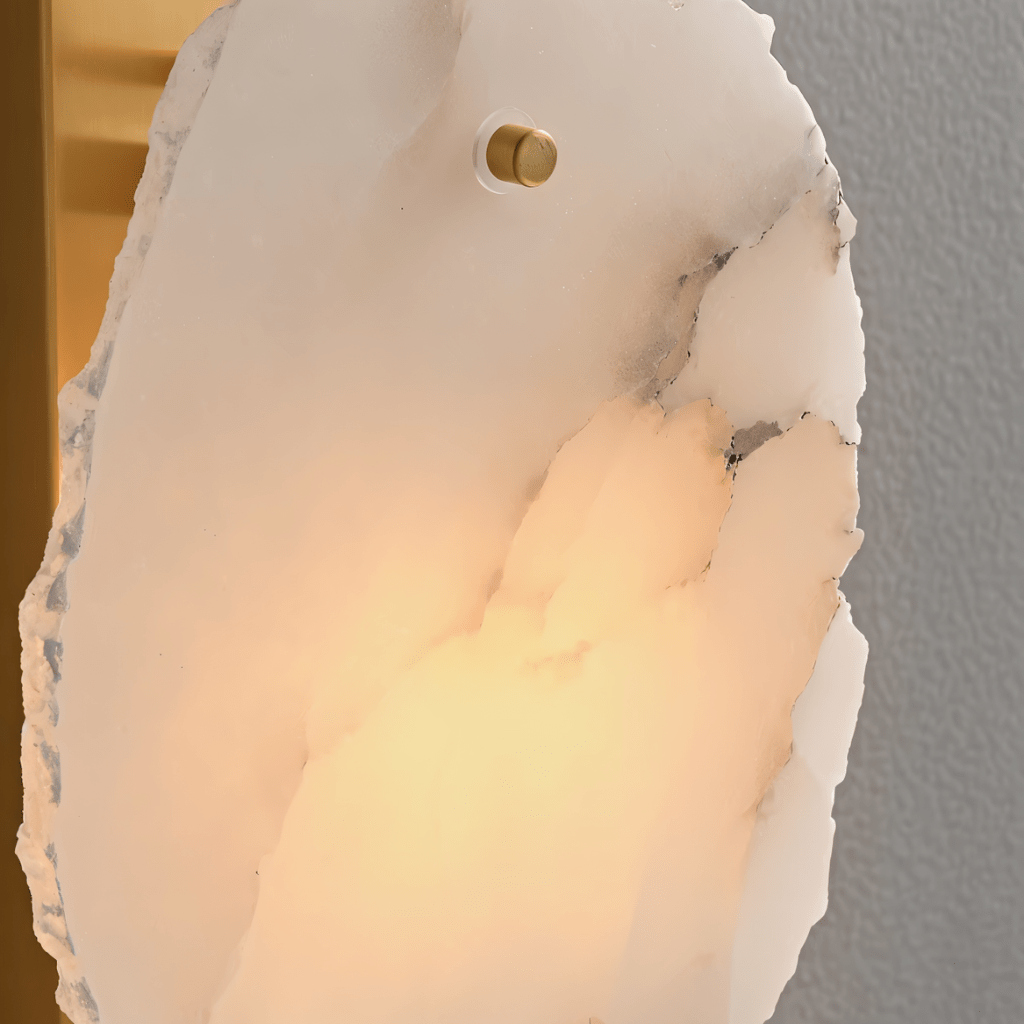 Clérachic wall lamp close-up of one veined alabaster panel, lit warm, with its brass pin and brass plate.