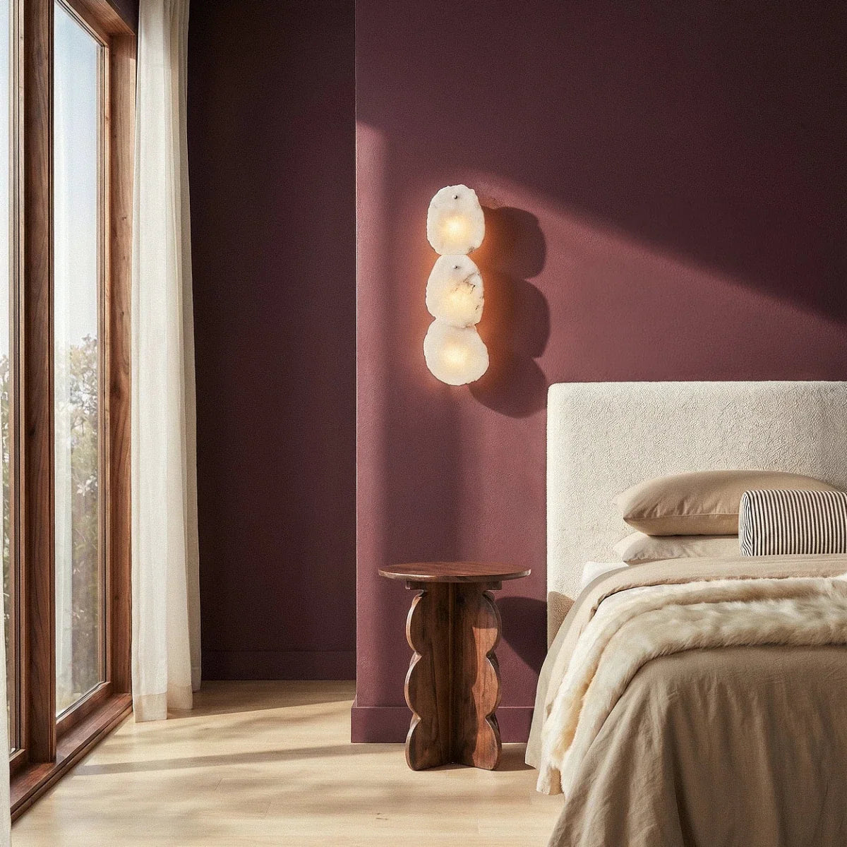Clérachic three-light alabaster wall lamp above a wooden side table in a plum bedroom beside a window.