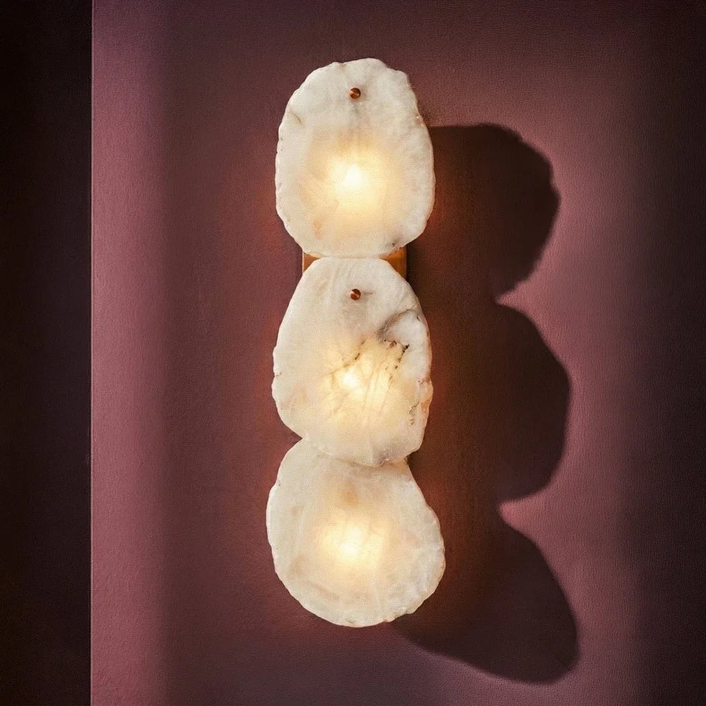 Clérachic three-light alabaster wall lamp glowing on a plum wall, casting soft rounded shadows.