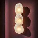 Clérachic three-light alabaster wall lamp glowing on a plum wall, casting soft rounded shadows.
