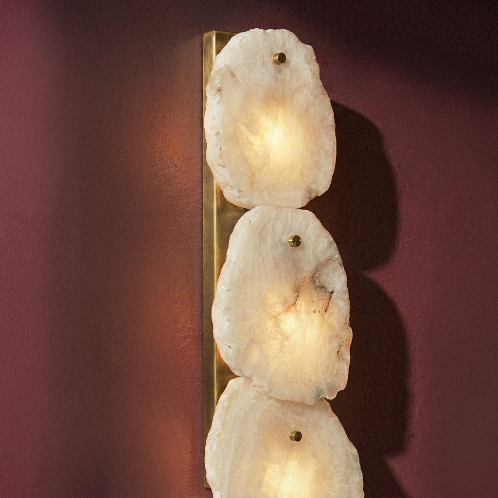 Clérachic alabaster wall lamp close-up on a plum wall, glowing marble panels pinned to a brass backplate.