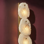 Clérachic alabaster wall lamp close-up on a plum wall, glowing marble panels pinned to a brass backplate.