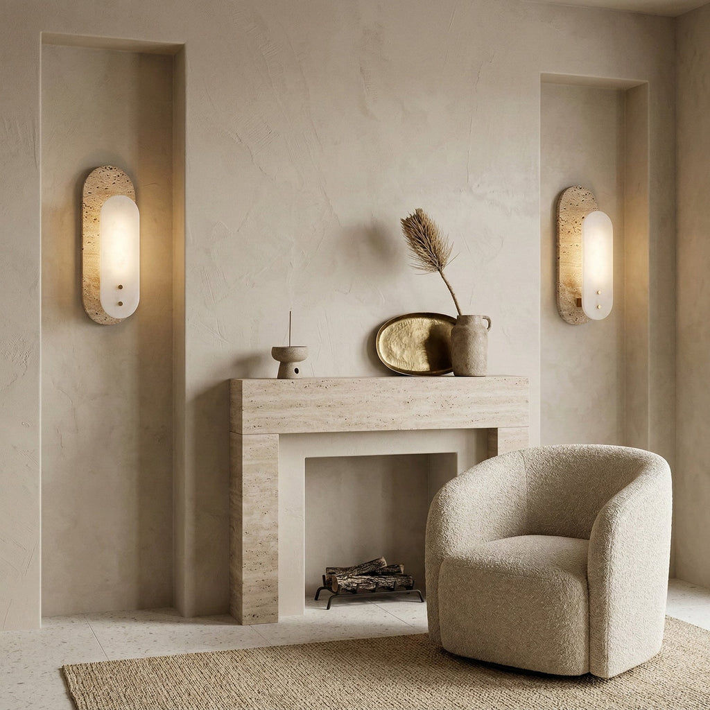 Two Clérachic wall lights glow either side of a plaster fireplace, with a cream bouclé armchair, a dried plume and a brass tray between them.
