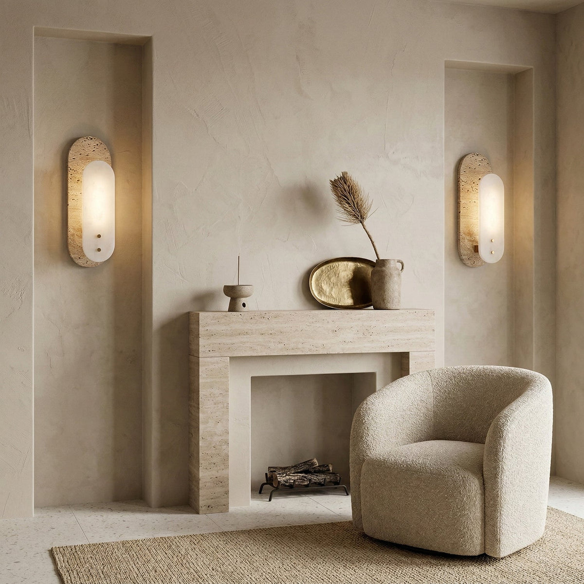Two Clérachic wall lights glow either side of a plaster fireplace, with a cream bouclé armchair, a dried plume and a brass tray between them.