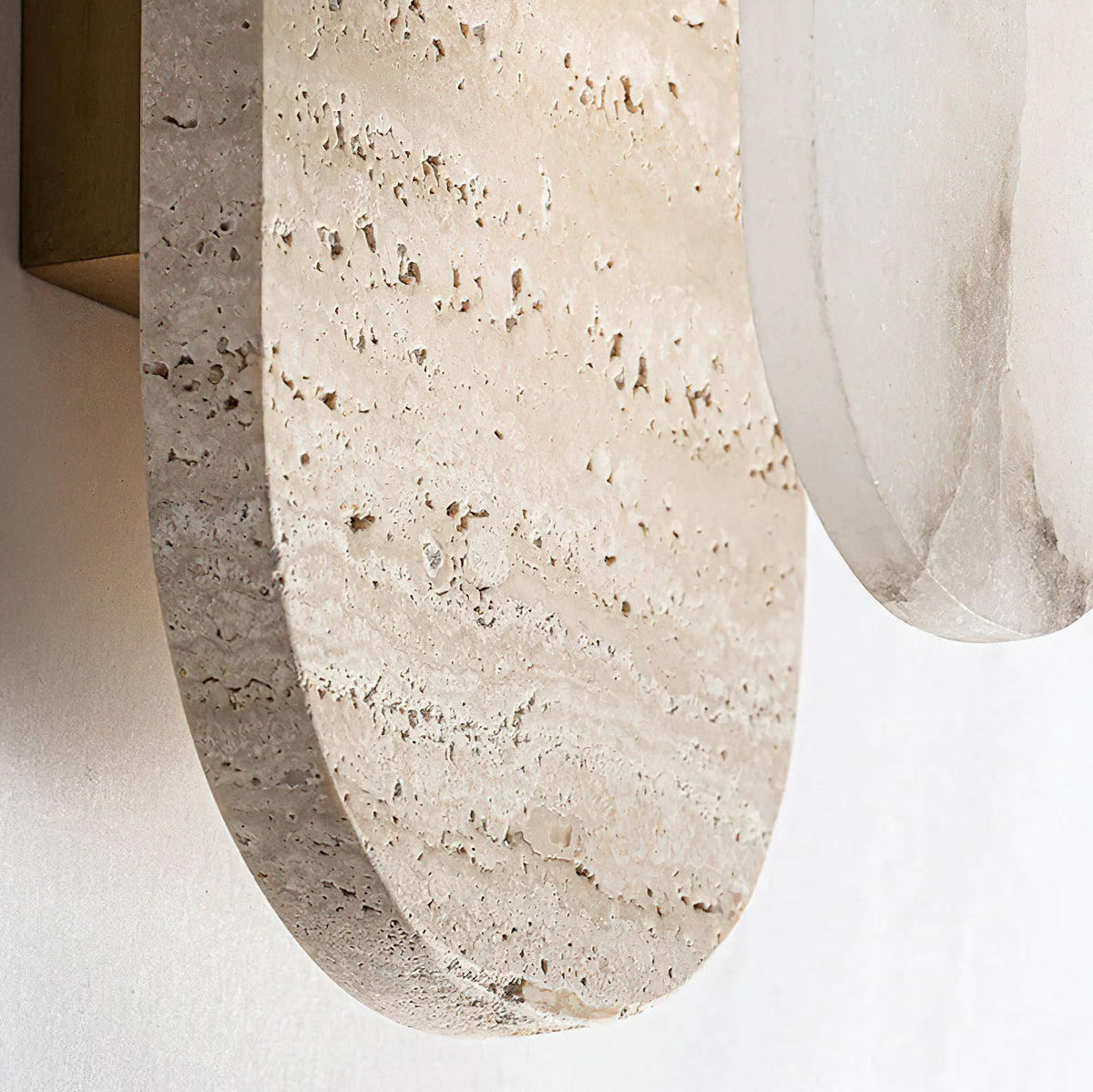 Close view of the pitted edge of the travertine plate on this Clérachic wall light, with the alabaster oval beside it.