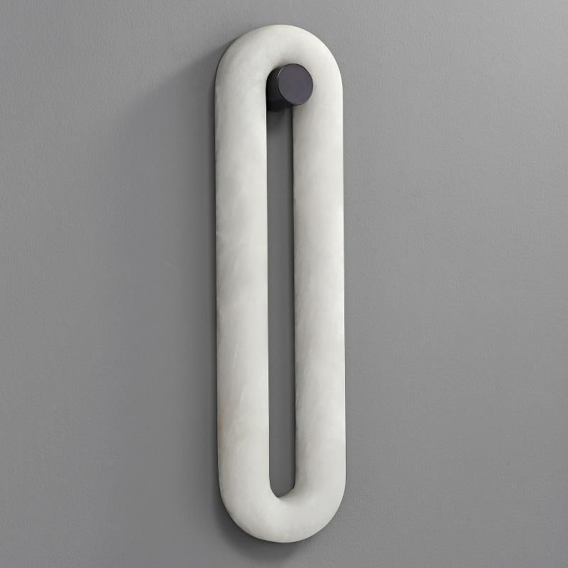 The taller Clérachic Alabaster Wall Sconce shown unlit, its slim white stone loop running down a plain grey wall.