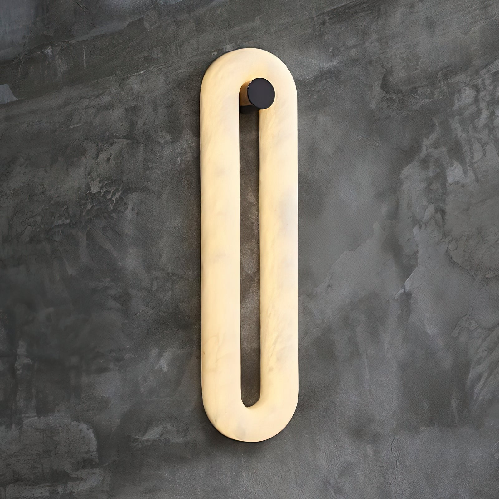 Clérachic Alabaster Wall Sconce lit on a raw concrete wall, warm light spreading evenly through the veined stone loop.