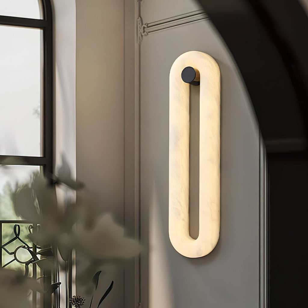 Clérachic Alabaster Wall Sconce lit beside an arched window, glowing softly on a panelled wall above a vase of foliage.