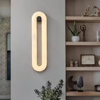 Clérachic Alabaster Wall Sconce lit beside open shelving, its warm oval of light set against a cool grey wall.