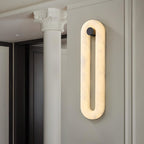 Clérachic Alabaster Wall Sconce lit in a hallway next to a classical column, the stone loop reading as a tall soft line.