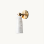 Brass and white Clérachic wall light with a rounded alabaster shade on a short arm and round backplate, on a plain off-white backdrop.