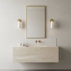 Two small Clérachic alabaster sconces either side of a tall brass-framed mirror above a floating travertine-look basin.