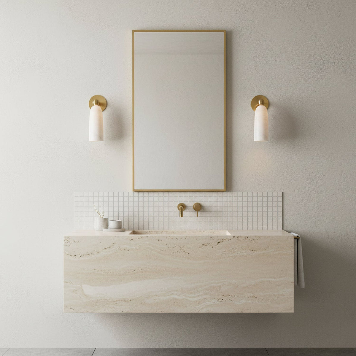 Two small Clérachic alabaster sconces either side of a tall brass-framed mirror above a floating travertine-look basin.
