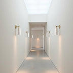 A row of small Clérachic alabaster wall lights along a long white corridor, each throwing a soft pool of light onto the wall.