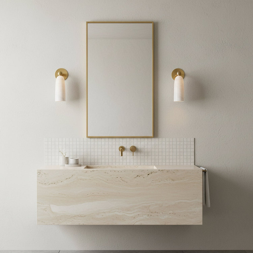 Brass-armed Clérachic sconces with white alabaster shades flanking a narrow gold-framed mirror over a stone vanity.