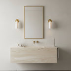 Brass-armed Clérachic sconces with white alabaster shades flanking a narrow gold-framed mirror over a stone vanity.