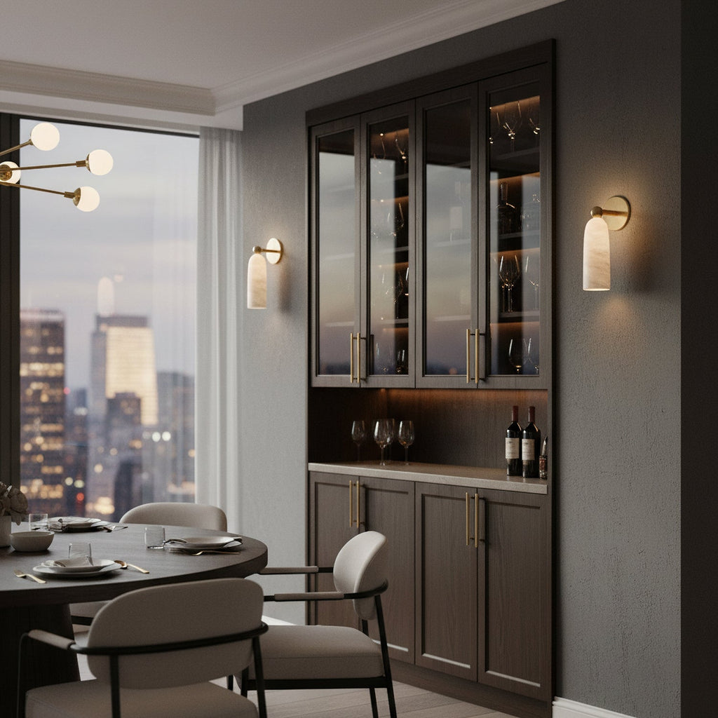 A Clérachic alabaster wall light on a dark dining-room wall, next to a glazed wine cabinet and a round table.