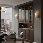 A Clérachic alabaster wall light on a dark dining-room wall, next to a glazed wine cabinet and a round table.