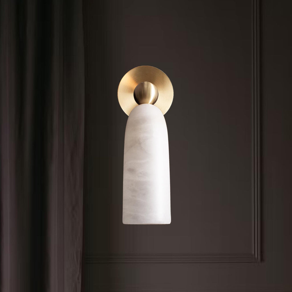 Front view of this Clérachic wall light, its brass disc backplate behind a pale alabaster shade, against a dark panelled wall.