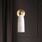 Front view of this Clérachic wall light, its brass disc backplate behind a pale alabaster shade, against a dark panelled wall.