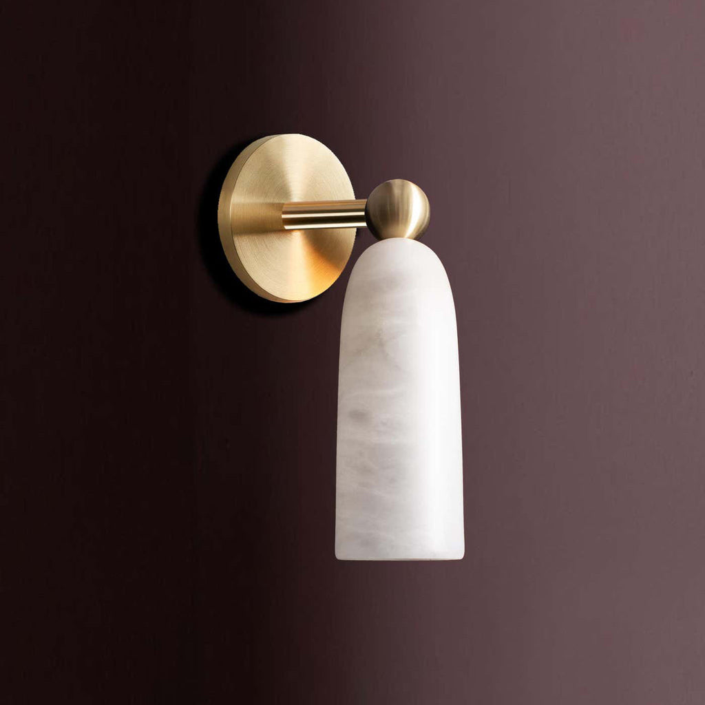 Side view of this Clérachic wall light with a brass arm and ball joint, its cylindrical alabaster shade on a deep plum wall.