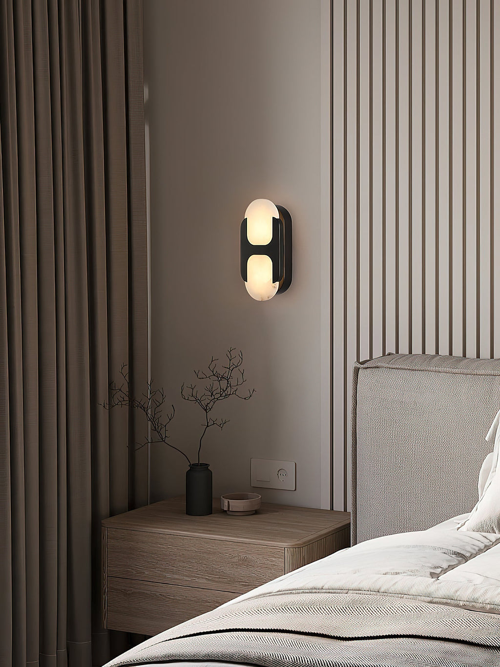Clérachic Alabaster Wall Sconce in black above a bedside table, giving a warm reading glow beside a fluted bedroom wall.