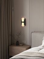 Clérachic Alabaster Wall Sconce in black above a bedside table, giving a warm reading glow beside a fluted bedroom wall.