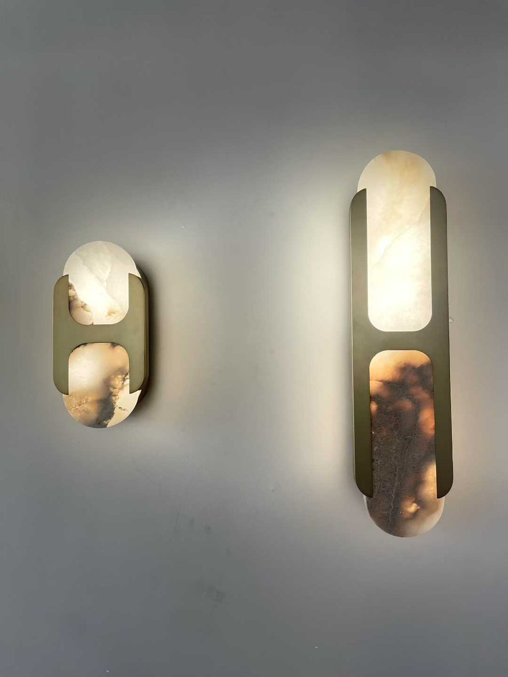 Both sizes of the Clérachic Alabaster Wall Sconce in brass, lit side by side so the honey and smoke veining in each panel shows.