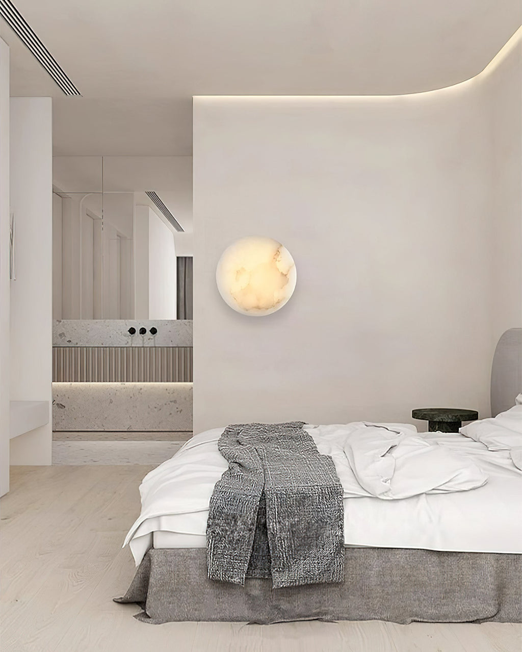 Clérachic Alabaster Wall Sconce lighting a pale bedroom wall beside a made bed, with the bathroom visible beyond.