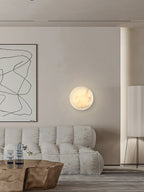 Clérachic Alabaster Wall Sconce lit beside a framed line drawing, above a soft tufted sofa in a greige living room.