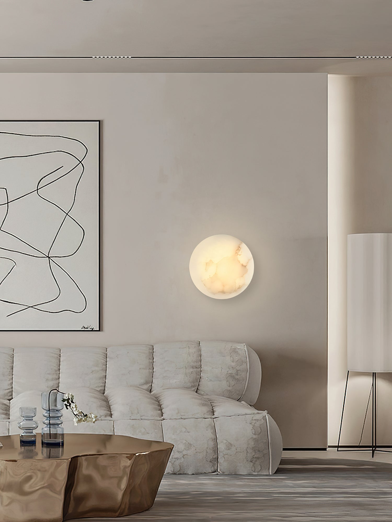 Clérachic Alabaster Wall Sconce lit beside a framed line drawing, above a soft tufted sofa in a greige living room.