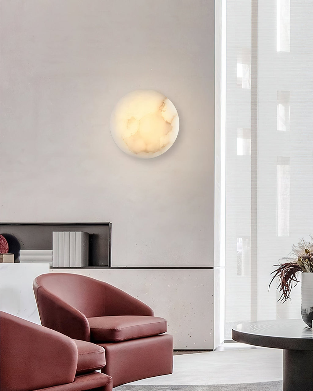 Clérachic Alabaster Wall Sconce glowing on a concrete lounge wall above two oxblood leather armchairs.