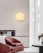 Clérachic Alabaster Wall Sconce glowing on a concrete lounge wall above two oxblood leather armchairs.