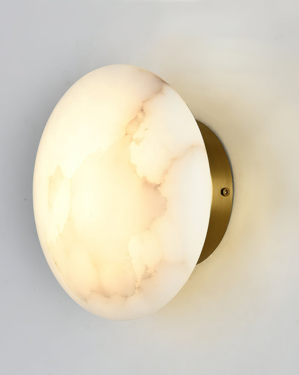 Angled close view of the Clérachic Alabaster Wall Sconce, brass backplate and fixing screw behind the lit stone.